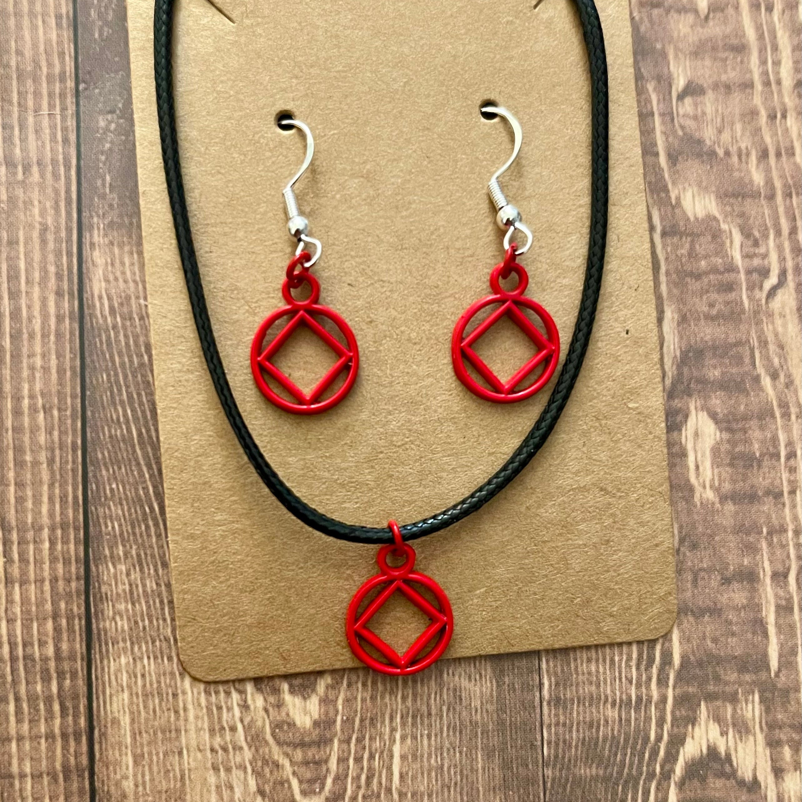Red AA pendant necklace and earrings on a brown card with a wooden background