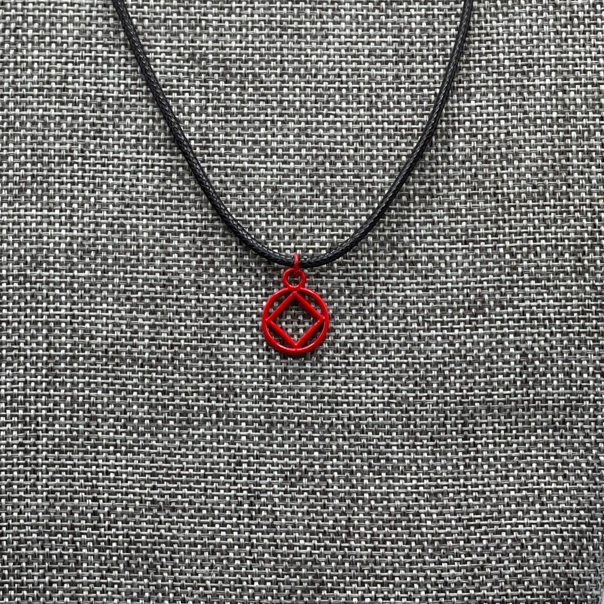 A red coated stainless steel Narcotics Anonymous symbol necklace displayed on a grey textured mannequin.