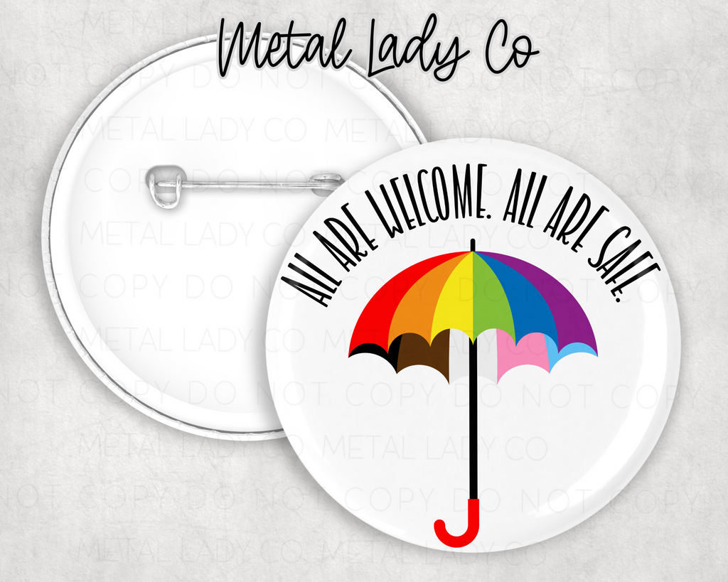 A round pinback button with an umbrella design and the text 'All are welcome!' on it, with a metallic ladies co. branding below.