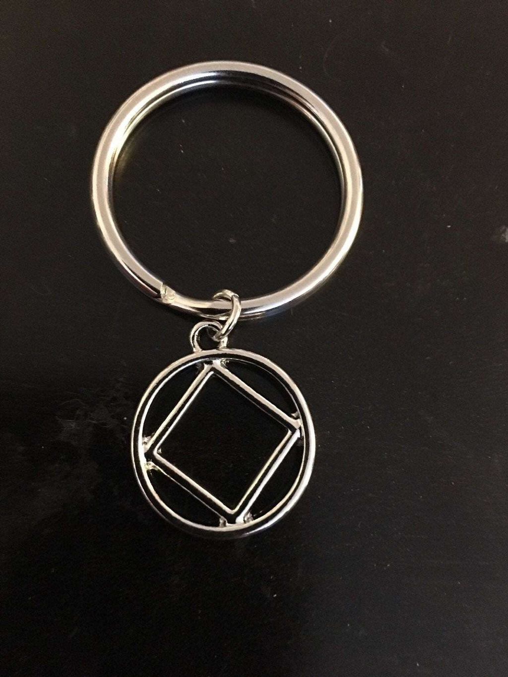 An upclose image of NA symbol attatched to a keychain with a jump ring on a black background