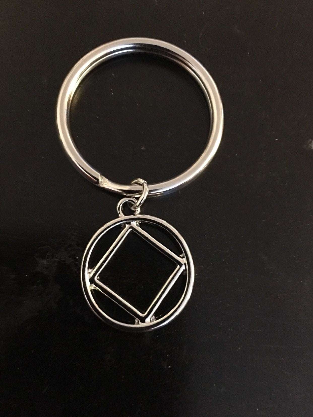 An upclose image of NA symbol attatched to a keychain with a jump ring on a black background