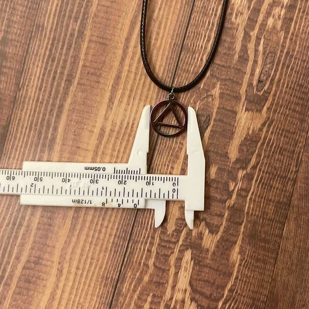 Necklace with a peace symbol pendant on a wooden surface with a ruler for scale.