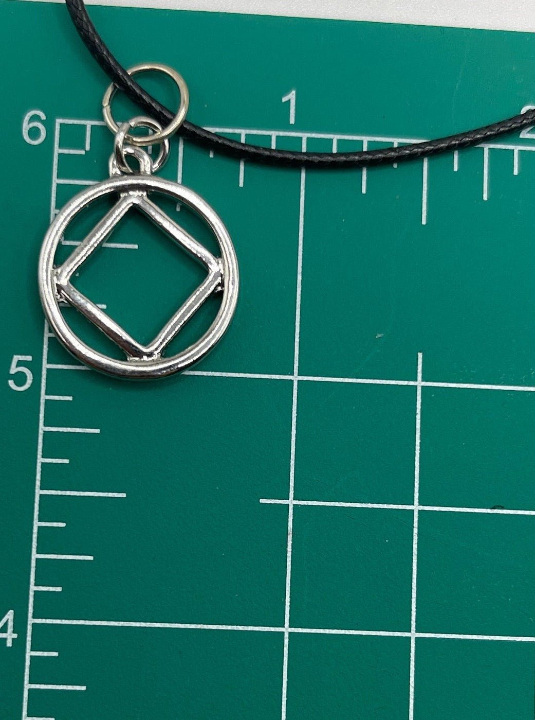 The NA symbol necklace on top of a measurement chart showing 3/4 inch in diameter measurements